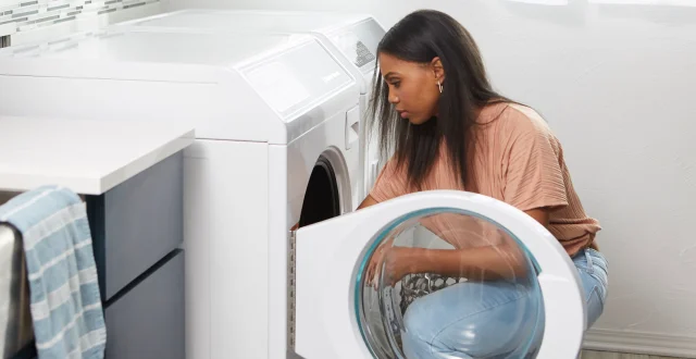 A woman is loading clothes into a Speed Queen washing machine, preparing for a laundry cycle.